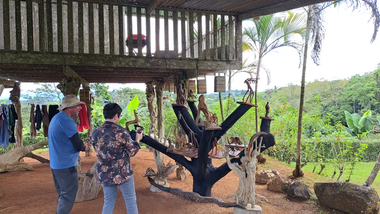 Unter einer Art Baumhaus sind mehrere aus Holz geschnitzte Tiere ausgestellt. Ein Mann und eine Frau schauen darauf. Sie fotografiert.