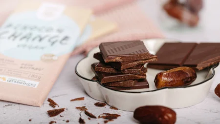 Nahaufnahme: Schokoladenstücke und Datteln liegen in und um eine Schale herum. Daneben ist unscharf eine Tafel Schokolade zu erkennen.