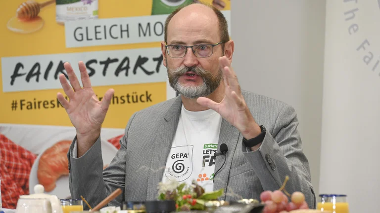GEPA-Gesch&auml;ftsf&uuml;hrer Peter Schaumberger spricht und gestikuliert. Hinter ihm sind GEPA-Banner aufgestellt mit der Aufschrift "Gleich morgens fair starten!"