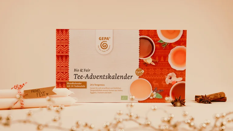 Der GEPA-Tee-Adventskalender arrangiert mit weißen Kerzen und einer Lichterkette im Vordergrund.