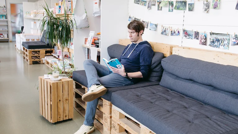 Junger Mann sitzt auf einer Bank in einem Geschäft und liest ein Buch