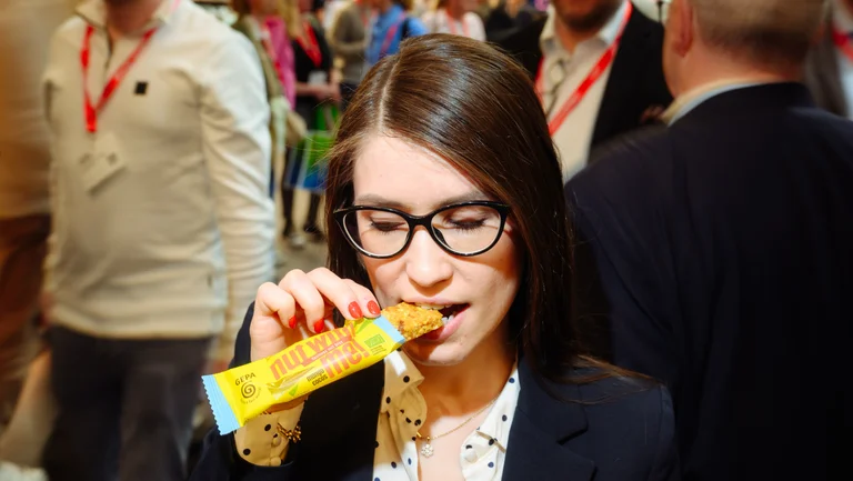 Junge Frau in einer Messehalle mit einem GEPA-Nussriegel &ldquo;Mango Cocos&rdquo;