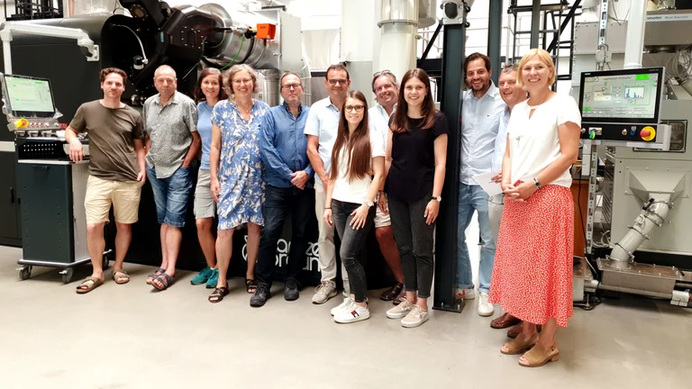 Zwölf Personen in der Produktionshalle der Kaffeerösterei Braun. Sie stehen nebeneinander und lächeln in die Kamera.