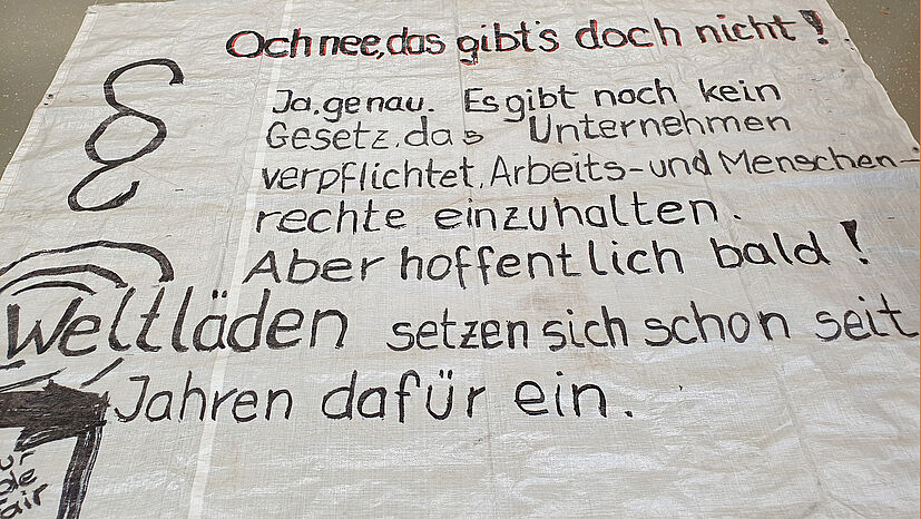 Das Ziel: Auf Fairen Handel aufmerksam machen. Obwohl sie bei der GEPA sozusagen „Heimspiel“ haben, ist schnell das Bodenplakat mit der Forderung nach dem Lieferkettengesetz ausgerollt.