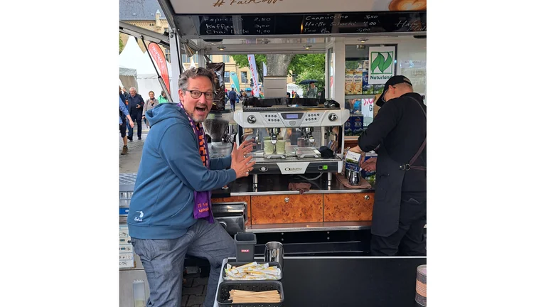 Eckart von Hirschhausen deutet euphorisch auf eine Kaffee-Ape hinter ihm.