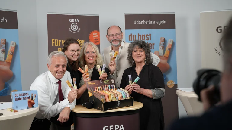 Gruppenbild nach der Jahrespressekonferenz 2024 der GEPA: Matthias Kroth, Alexandra Bleuel, Barbara Schimmelpfennig, Peter Schaumberger und Andrea Fütterer halten GEPA-Schokoriegel in die Kamera und lächeln