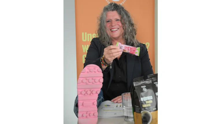Andrea F&uuml;tterer h&auml;lt einen pinken Nussriegel in der Hand und zeigt ihre knallpinke Schuhsohle in die Kamera.