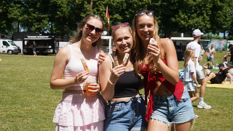 Drei junge Frauen auf der Wiese eines Festivalgel&auml;ndes. Sie halten GEPA-Schokoriegel und l&auml;cheln in die Kamera.