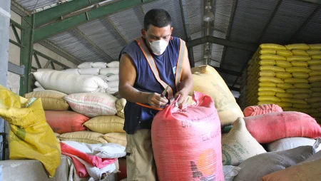 Mann steht in einer Lagerhalle mit vielen S&auml;cken darin. Er ist gerade dabei, einen der S&auml;cke zuzubinden.