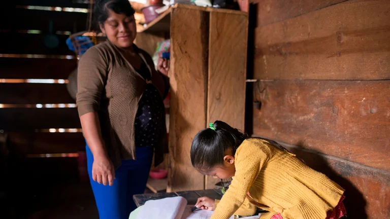 Frau blickt auf ihre Tochter, die gerade Schulaufgaben macht