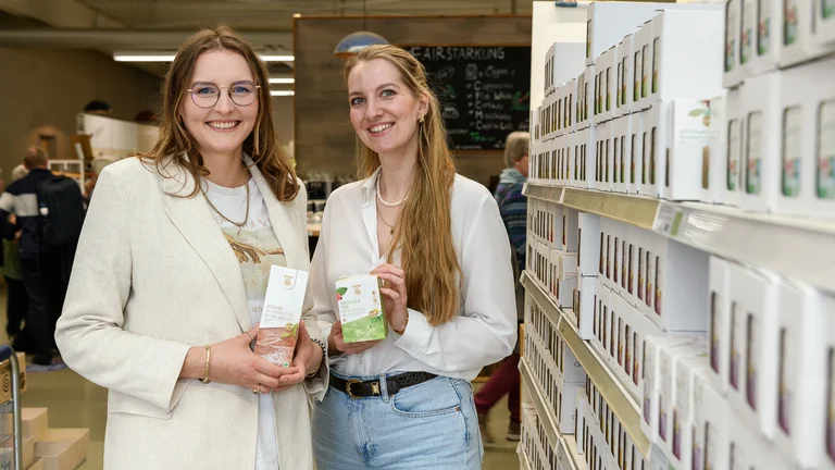 Zwei junge Frauen stehen am Teeregal im GEPA-Store. Sie l&auml;cheln in die Kamera und halten je eine Packung Tee in der Hand.