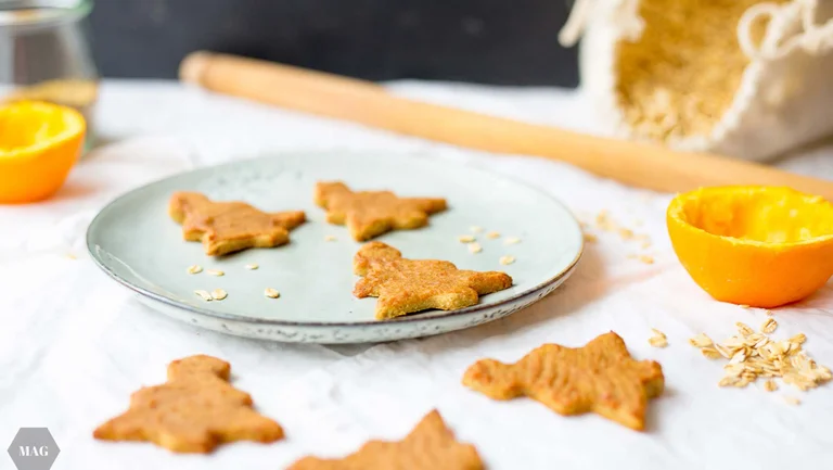Plätzchen in Form von Tannenbäumen auf einem Teller, dekoriert mit einer Orange und Haferflocken