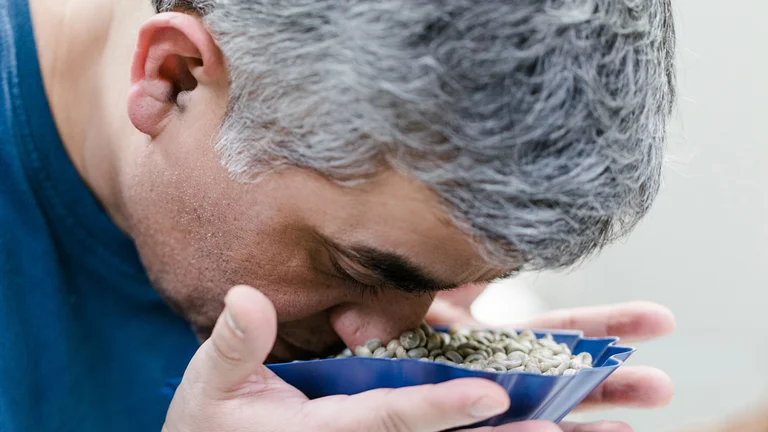 Nahaufnahme wie Kleber Cruz-Garcia seine Nase in eine Schale mit Kaffeebohnen h&auml;lt.