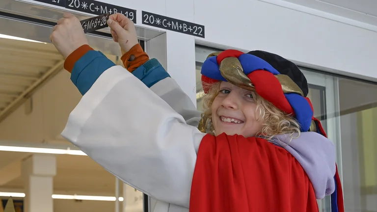 Sternsinger-Junge beim Aufkleben eines Segensaufklebers f&uuml;r 2026. Es h&auml;ngen schon weitere Aufkleber aus fr&uuml;heren Jahren dort.