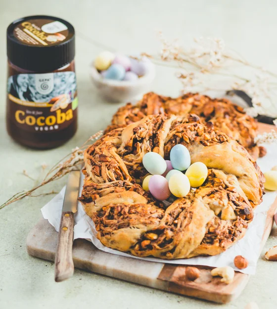 Ein Glas GEPA-Schokocreme neben einem Hefezopf dekoriert mit bunten Eiern