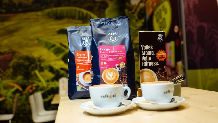 Zwei GEPA-Kaffeepackungen der Sorten &ldquo;Fuego&rdquo; und &ldquo;Grano&rdquo;, davor zwei Tassen mit Cappuccino und Latte-Art.