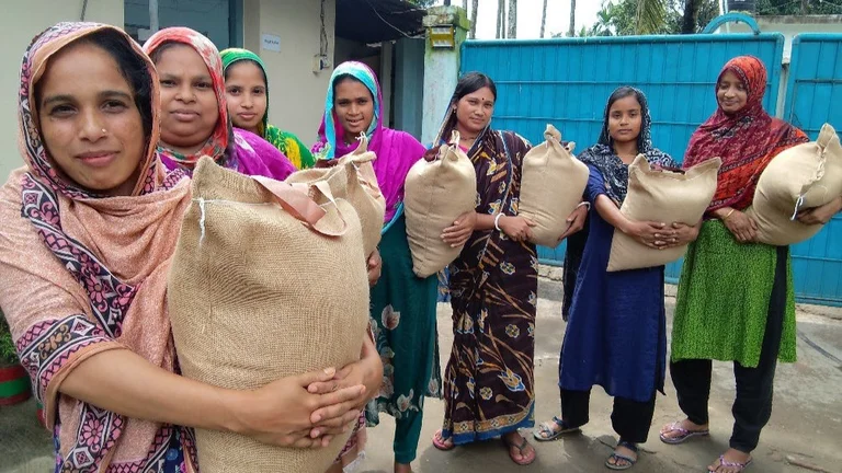 Sieben Frauen in Saris halten je einen Sack Reis und schauen in die Kamera