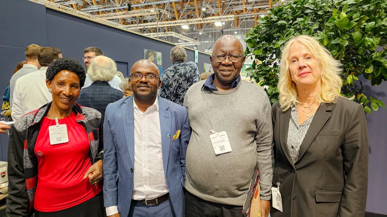 Zwei M&auml;nner und zwei Frauen auf einem Messegel&auml;nde schauen in die Kamera. An einer Messewand im Hintergrund sind Naturland-Logos zu erkennen.