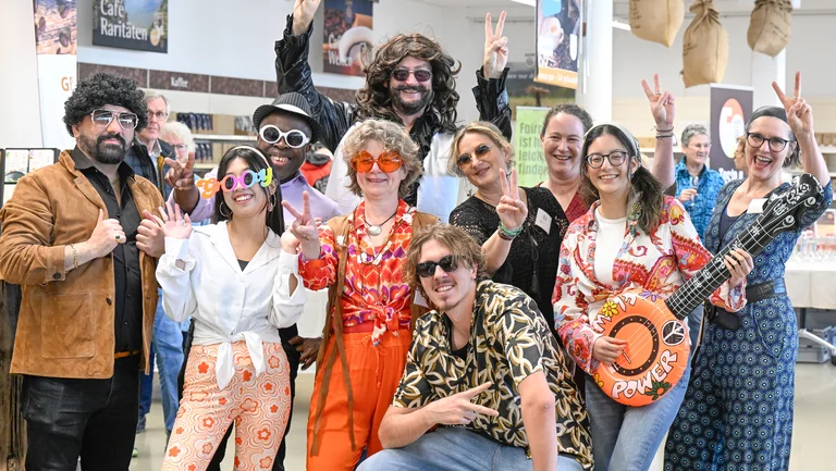Gruppenfoto von GEPA-Mitarbeitenden im 70er-Jahre-Stil: bunt, Flower Power, Sonnenbrillen, eine bunte Gitarre.