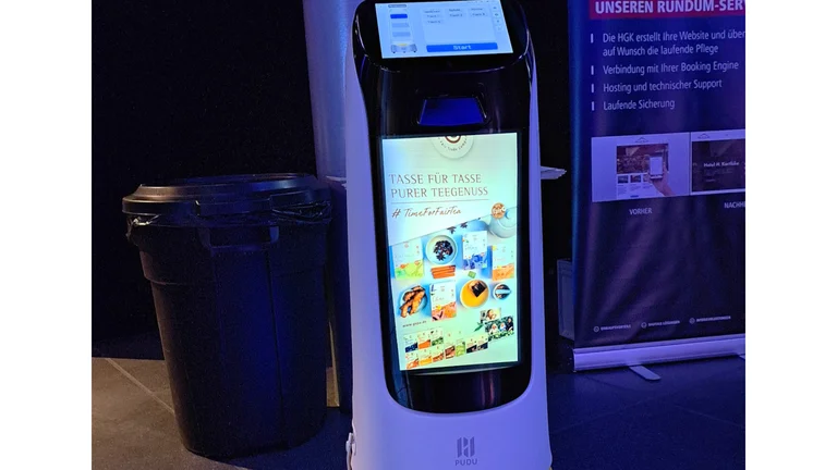 In einem dunklen Raum steht eine Art Roboter mit gro&szlig;em Display an der Front. Darauf ein arrangiertes Bild mit Tee und GEPA-Teeprodukten. Dar&uuml;ber der Schriftzug "Tasse f&uuml;r Tasse fairer Teegenuss. #Timeforfairtea"