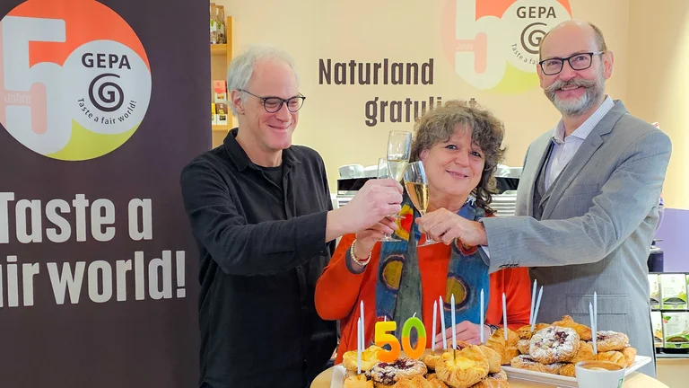 Matthias Fiedler, Geschäftsführer des Forum Fairer Handel, Andrea Fütterer (GEPA-Abteilung Grundsatz und Politik) und GEPA-Geschäftsführer Peter Schaumberger stoßen mit Sekt auf der BIOFACH 2025 an.