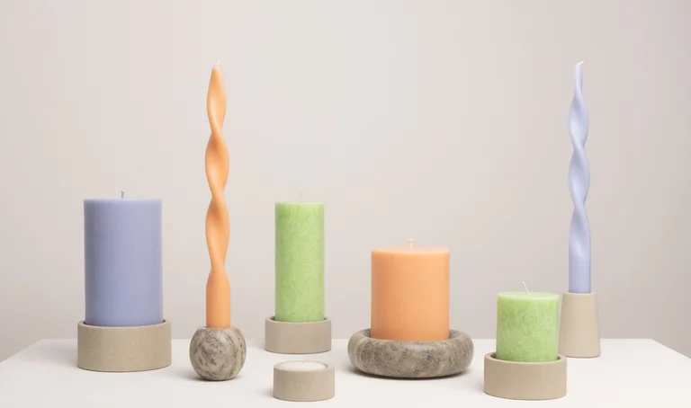 Zusammenstellung von GEPA-Kerzen in verschiedenen Formen in den Farben blasslila, pfirsich und leuchtendem hellgrün in verschiedenen Kerzenhaltern aus Palewa- oder Mintstein.