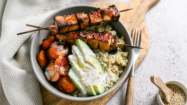Bowl von oben mit Tempeh-Spießen, Avocadoscheiben, Quinoa und Soße