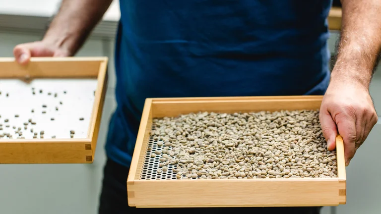 Nahaufnahme eines quadratischen Siebes mit Holzrahmen, das in einer Hand gehalten wird.