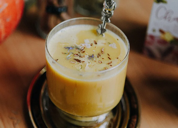 Glasbecher mit Kürbis-Chai-Latte, aus dem ein Löffel guckt