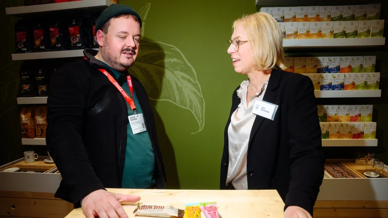 Gespr&auml;ch am Messestand, zwei Personen stehen an Holztisch und unterhalten sich.