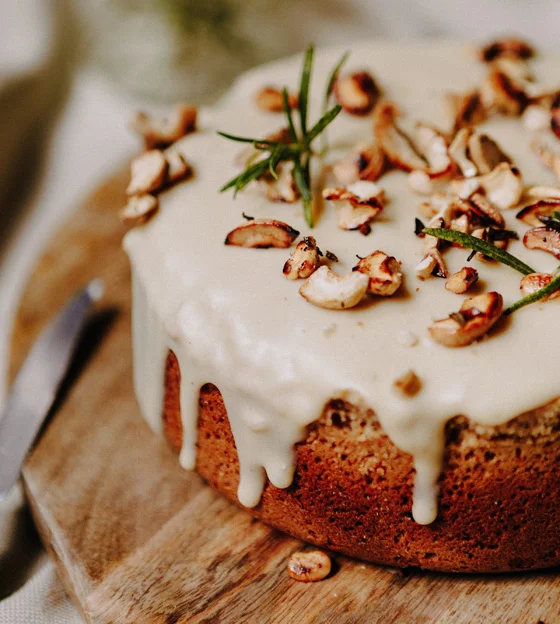Runder Kuchen mit reichlich Glasur, bestreut mit gerösteten Nüssen, auf einem Holzbrett.