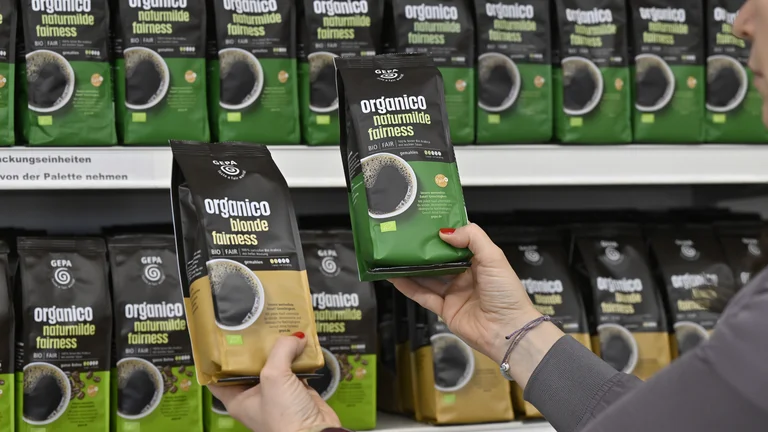 Zwei Hände halten je ein Päckchen „organico naturmilde fairness" und „organico blonde fairness", im Hintergrund ein Regal mit Organico-Päckchen verschiedener Varianten.