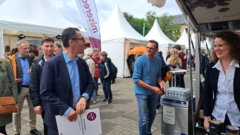 Cem &Ouml;zdemir auf einem Messegel&auml;nde im Freien. Er ruft einem Mann etwas zu. Um sie herum sieht man viele Messebesucher.