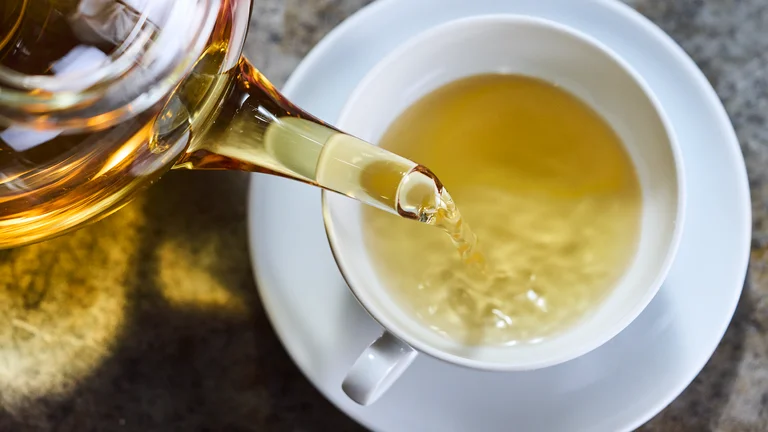 Nahaufnahme: Hellgrüner Tee wird aus einer Glaskanne in eine weiße Tasse gegossen.