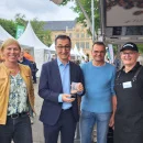 Cem Özdemir und drei GEPA-Mitarbeiter*innen auf einem Messegeländer im Freien. Sie lächeln in die Kamera.