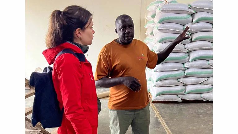 Mann und Frau in einem Lagerraum, in dem sich S&auml;cke stapeln. Er erkl&auml;rt ihr etwas.