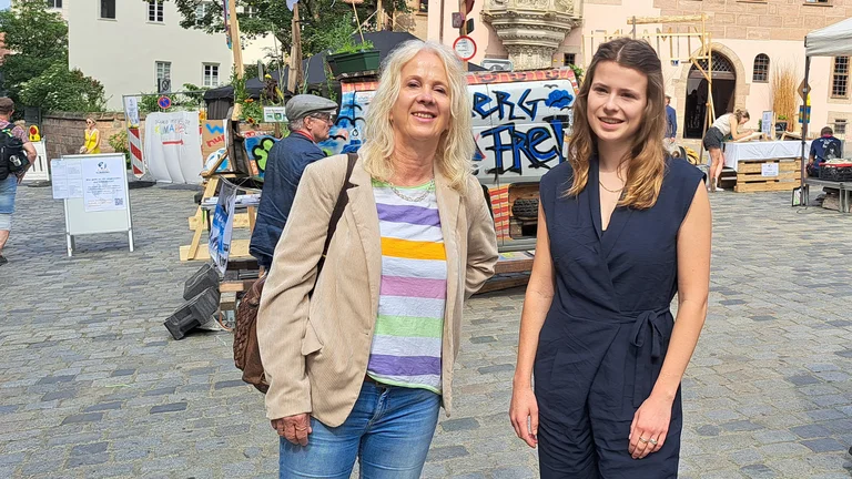 GEPA-Pressesprecherin Barbara Schimmelpfennig und Luisa Neubauer stehen nebeneinander auf einem gepflasterten Platz im Freien und l&auml;cheln in die Kamera. Hinter ihnen ein bunt bemalter Van.