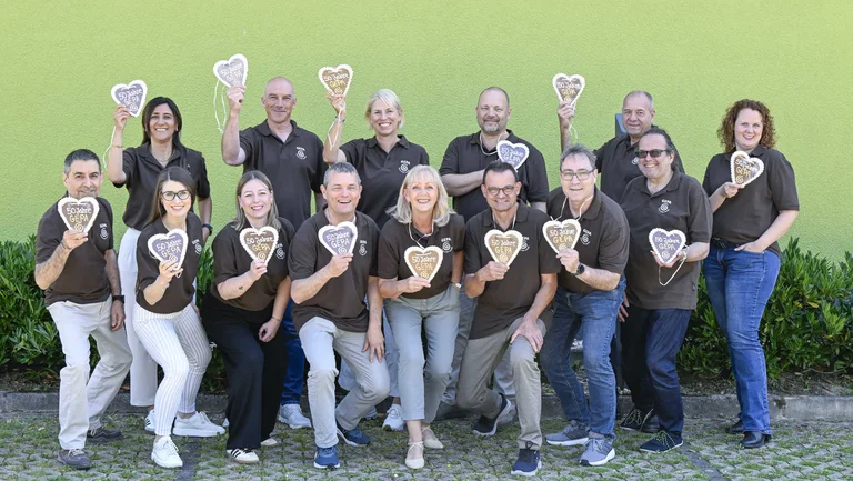 Vierzehn Erwachsene in braunen T-Shirts mit GEPA-Logo l&auml;cheln in die Kamera. Jede*r h&auml;lt ein Lebkuchenherz in die Kamera, auf dem "50 Jahre GEPA" steht.
