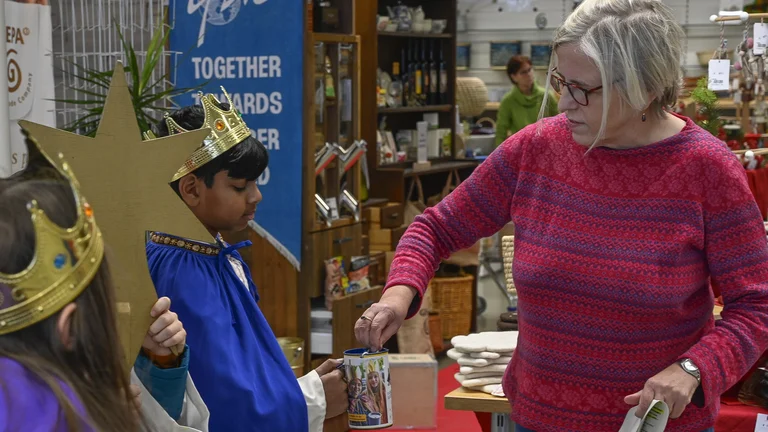 Frau in einem Gesch&auml;ft gibt einem als Sternsinger verkleideten Junge etwas in seine Spendendose.