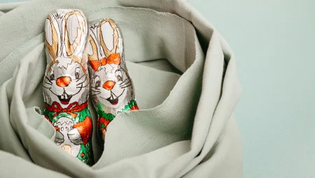 Zwei verpackte Schokoladenhasen schauen aus einem Tuch, in das sie eingewickelt sind.