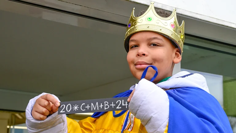 Als Sternsinger verkleideter Junge mit einer Krone h&auml;lt einen Sticker mit dem Segen der Sternsinger: 20*C+M+B+24