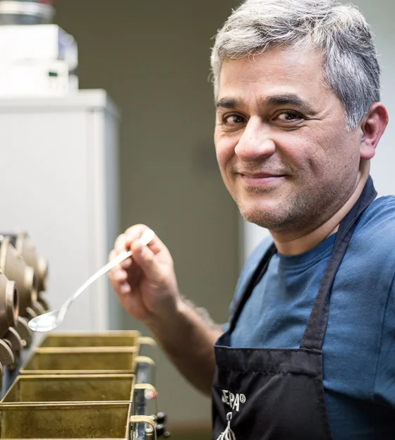 Porträtfoto Kleber Cruz-Garcia neben den Kaffeeröstern im GEPA-Kaffeelabor.
