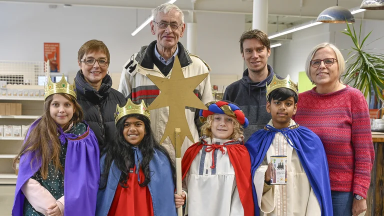 Gruppenbild von vier Sternsinger-Kindern (zwei Jungen, zwei M&auml;dchen) mit vier Erwachsenen in einem Lebensmittelgesch&auml;ft. Sie l&auml;cheln in die Kamera.