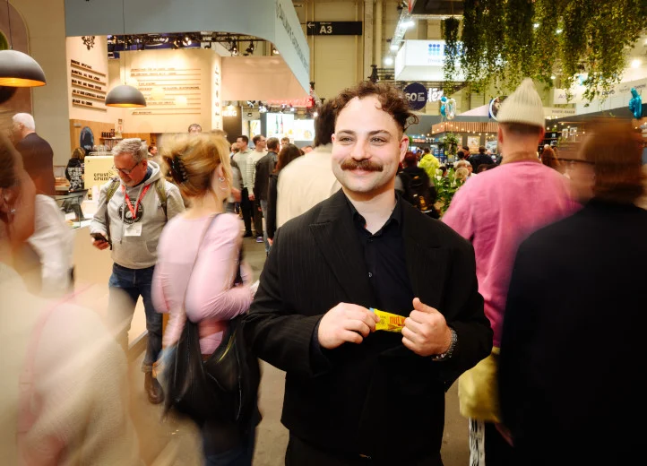 Junger Mann l&auml;uft durch eine Messehalle und hat einen GEPA-Nussriegel in der Hand. Um ihn herum verschwommen die Menschenmenge.