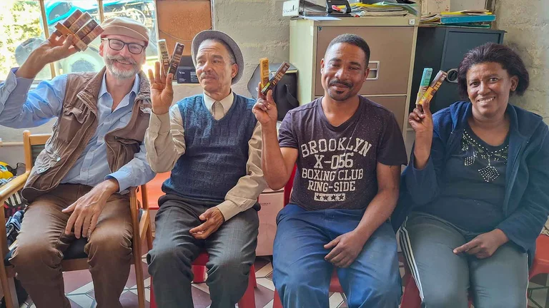 Vier Menschen sitzen auf Stühlen, halten mit je einer Hand GEPA-Riegel in die Höhe und lächeln. Links sitzt GEPA-Geschäftsführer Peter Schaumberger