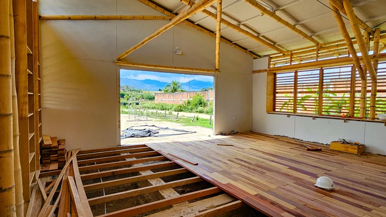 Innenansicht von einem Klassenraum im Bau. Stützpfeiler unter dem Dach sind aus Bambus. Der Boden ist noch nicht vollständig gedeckt.