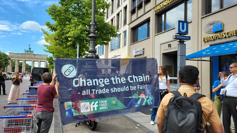 Menschen tragen ein Banner auf dem "Change The Chain" steht, im Hintergrund das Brandenburger Tor.