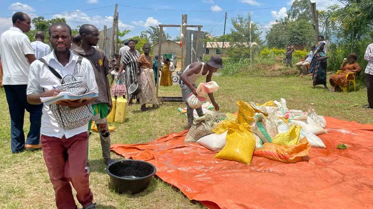Eine Grasfl&auml;che an einem Stra&szlig;enrand. Auf der Wiese ist eine Plane mit S&auml;cken darauf ausgelegt. Menschen stehen und sitzen im Umkreis der Plane