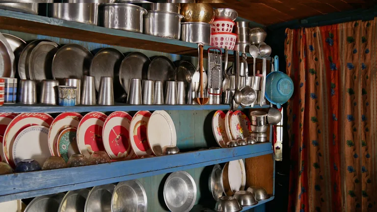 Metallteller und -Becher sowie gemustertes Geschirr in einem blauen, schmalen Regal.