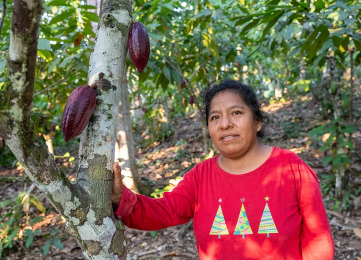 Eine Kakaobäuerin steht an einem Kakaobaum im Wald